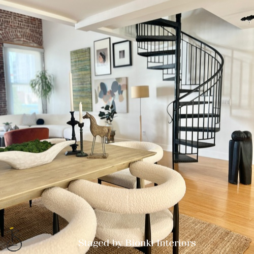 Luxury vacant home staging featuring an open-concept dining area with sculptural seating, warm wood tones, and a statement spiral staircase that highlights architectural character and flow. Staged by Bionki Interiors in Southern California.