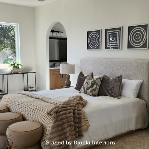 Luxury primary bedroom staging with soft neutral bedding, layered textiles, and balanced furniture placement designed to create an inviting retreat. Staged by Bionki Interiors.