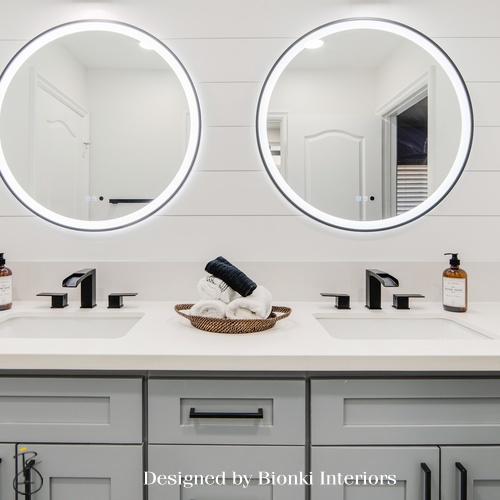 Custom bathroom design featuring a double vanity with matte black fixtures and illuminated mirrors. Designed by Bionki Interiors.