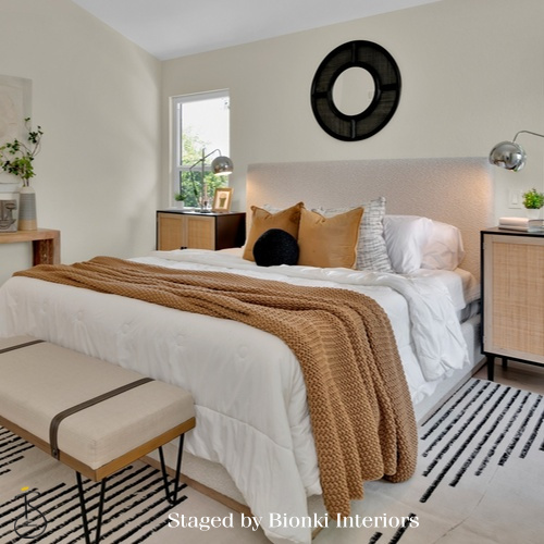 Luxury primary bedroom staging featuring layered neutral bedding and warm textile accents designed to create a calm and inviting retreat. Staged by Bionki Interiors.