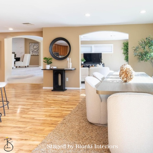 Luxury open-concept home staging featuring cohesive flow between living and dining areas with warm wood flooring. Staged by Bionki Interiors.